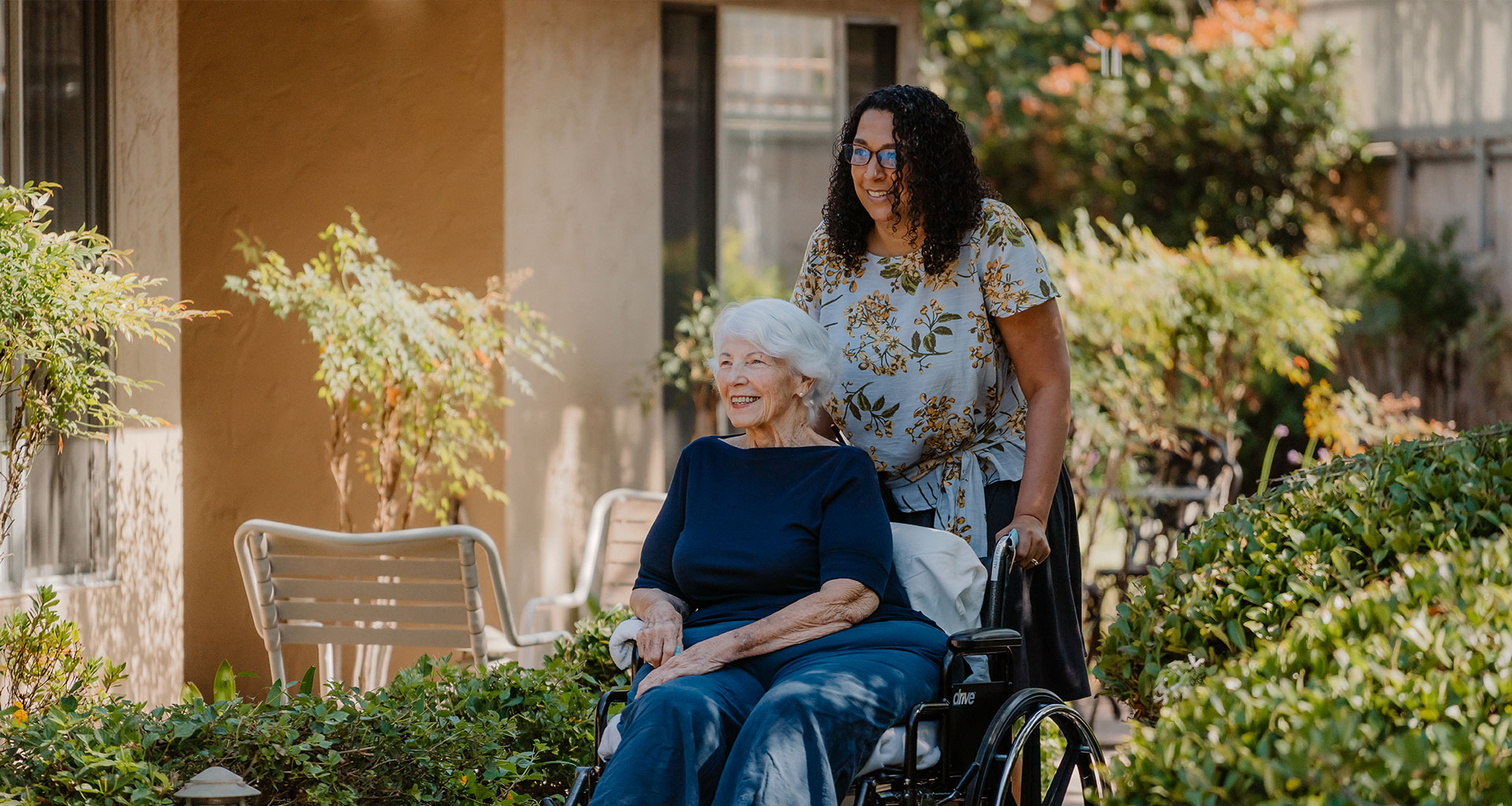 A caretaker pushes a senior woman in a wheelchair as they talk