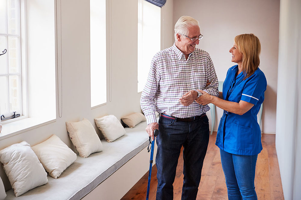 Senior man and a his nurse walk down a hall and talk