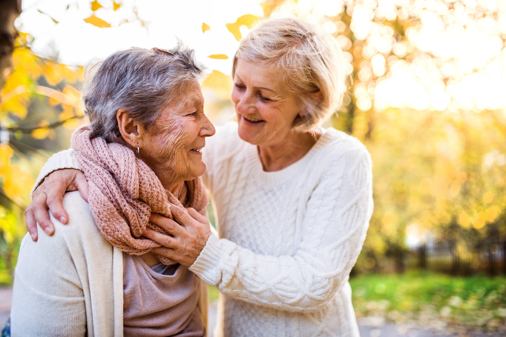 Two senior women walk outdoors and chat