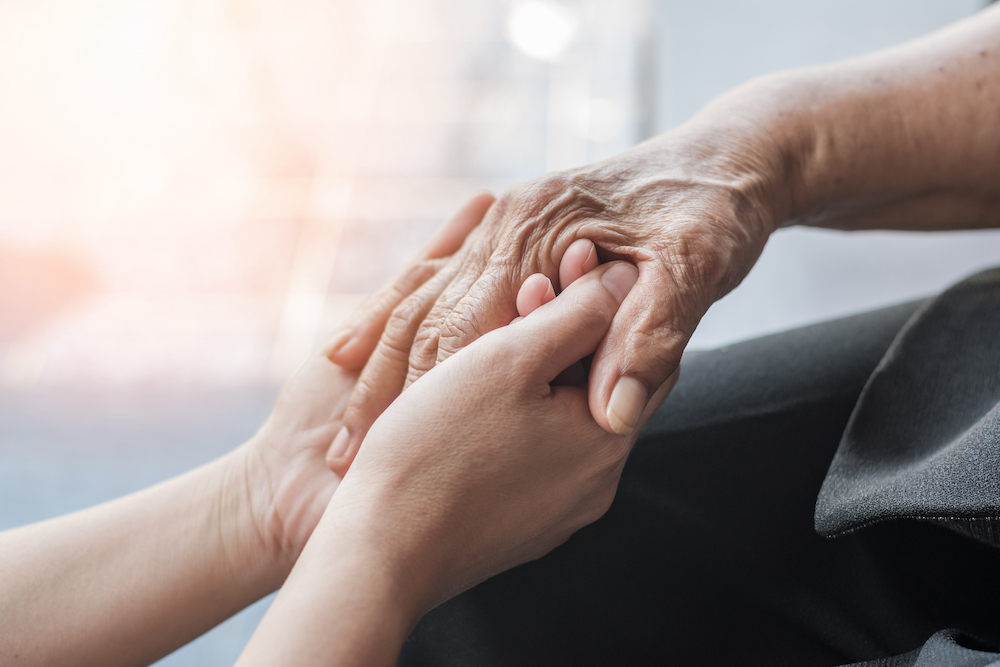 A senior and caregiver hold hands